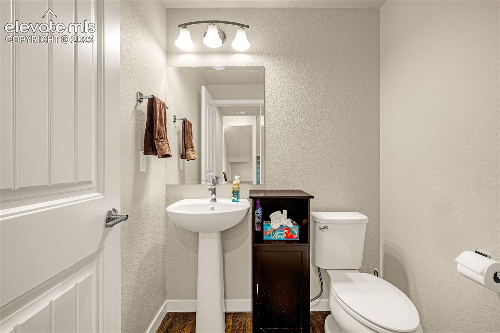 Main level powder room featuring a pedestal sink, wall-mounted mirror, three-light fixture, and wood-finish flooring