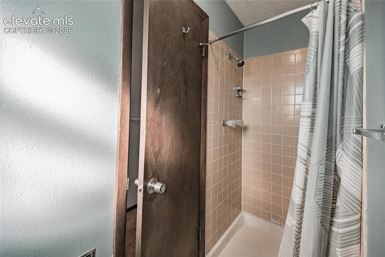 Shower stall with light-toned ceramic tile surround, wall-mounted showerhead, and integrated metal hardware