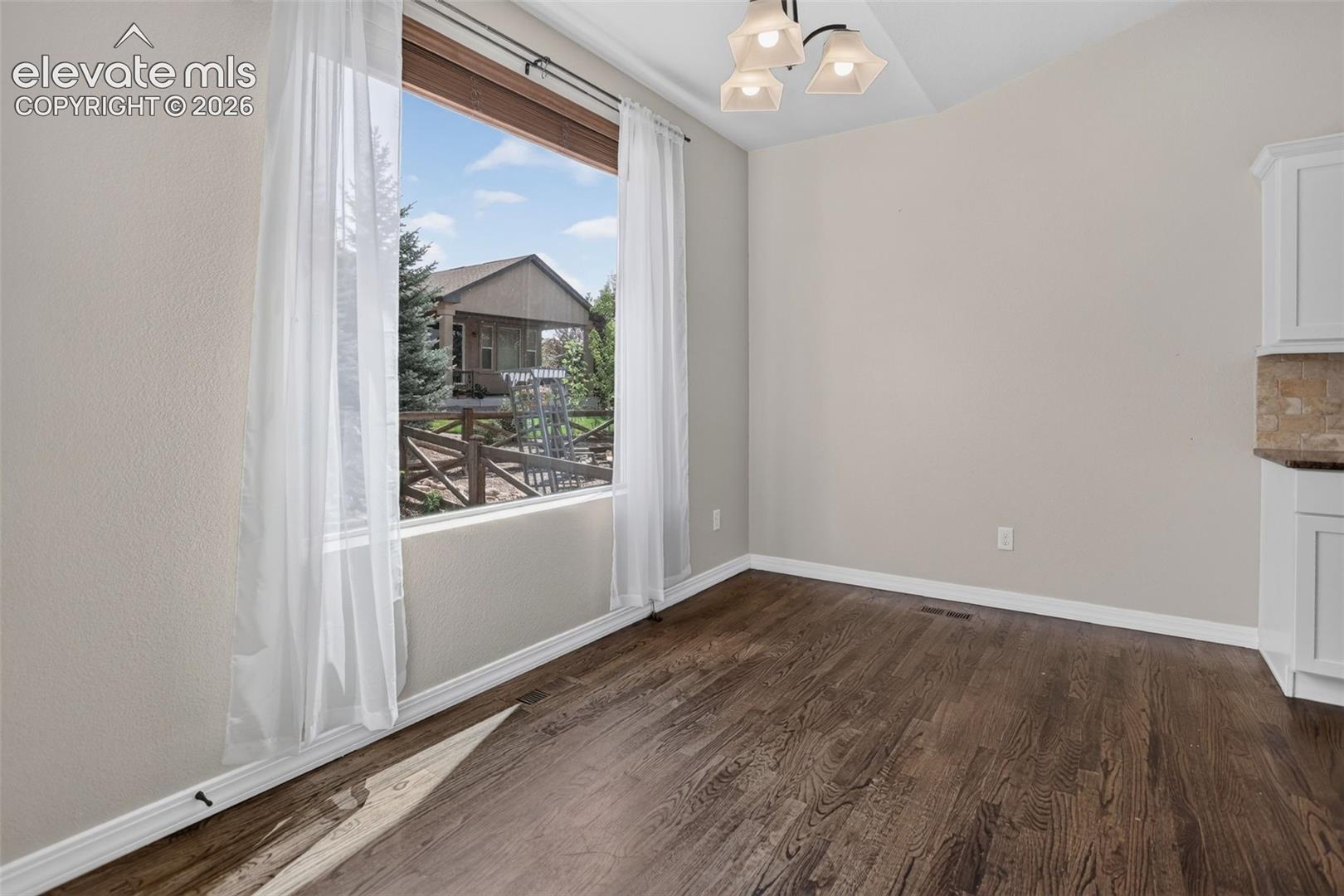 Vaulted ceiling with an attached light fixture, wood-finish flooring, and a large picture window
