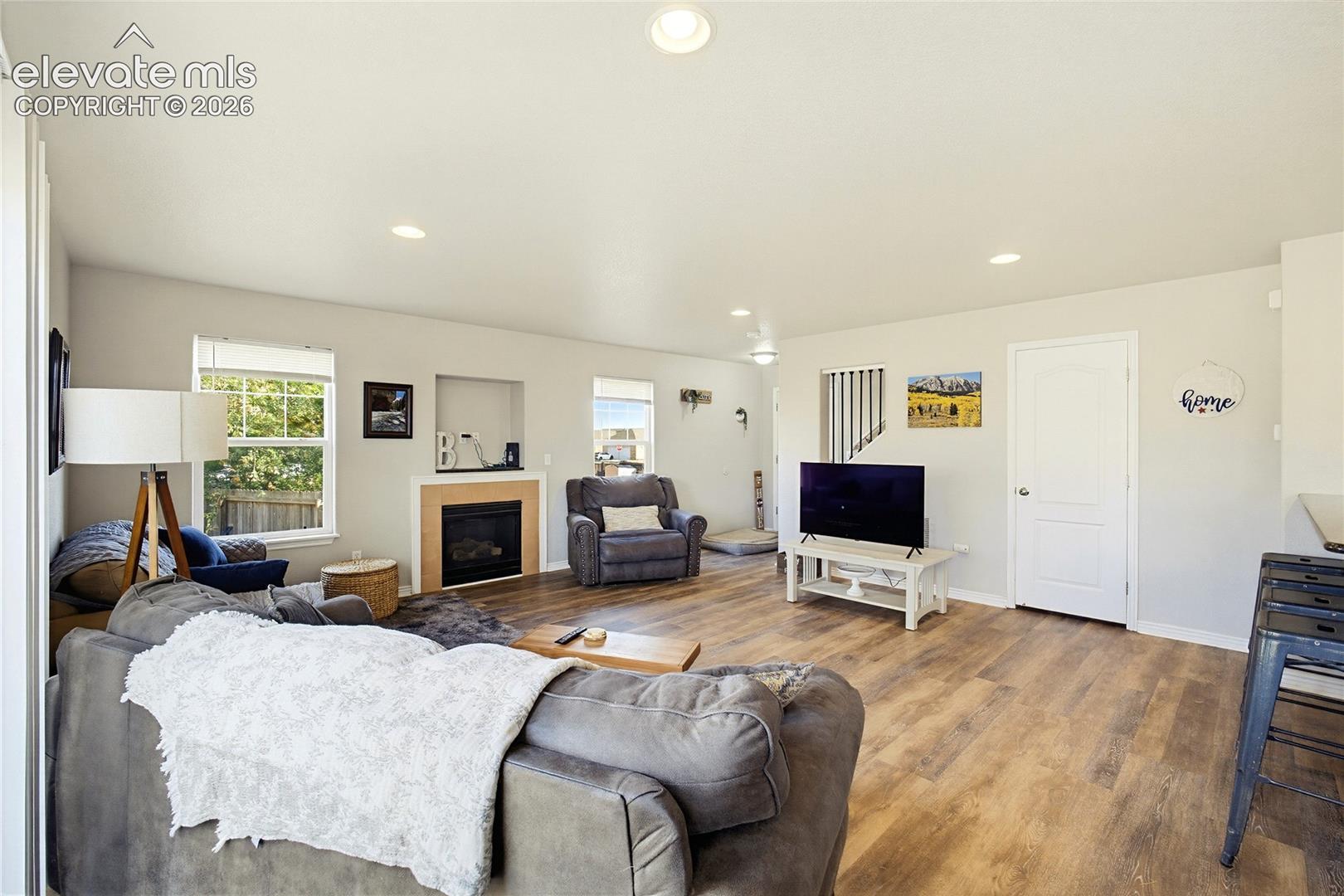 Open-concept living space featuring wood-finish flooring, recessed lighting, and a built-in fireplace with a stone-surround mantel
