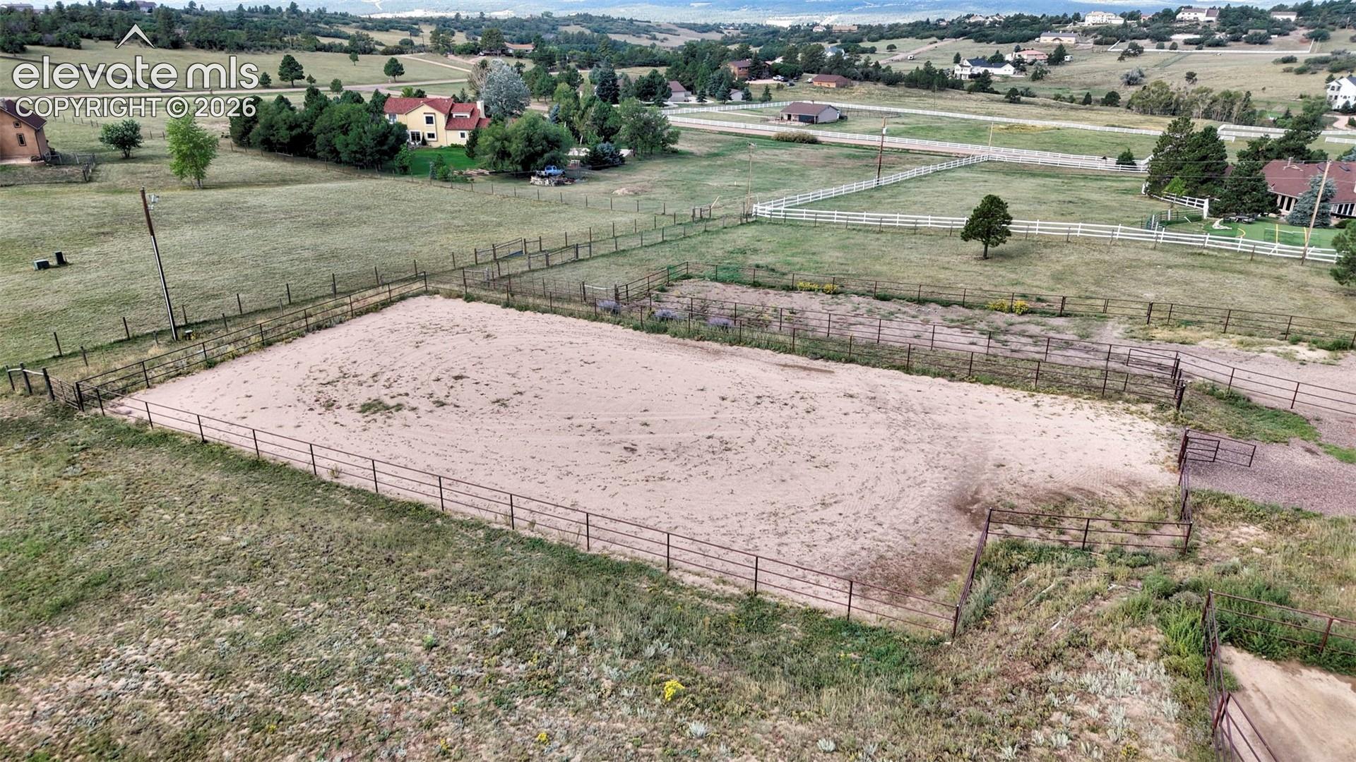 Fenced equestrian arena with granite footing, surrounded by expansive grassy areas and comprehensive fencing