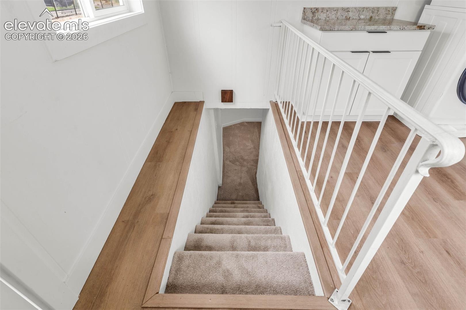 Staircase with carpeted treads, white metal handrail, wood-finish flooring, and built-in white cabinetry with stone-finish countertops