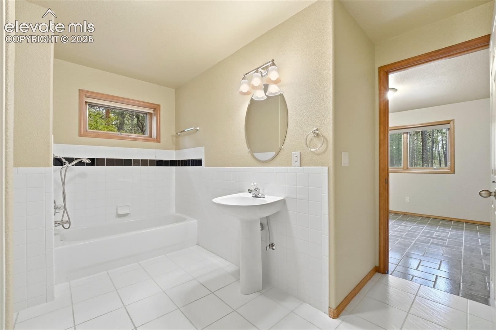 Bathroom featuring a pedestal sink, oval mirror with vanity lighting, and a bathtub with white subway tile surround and a black accent border