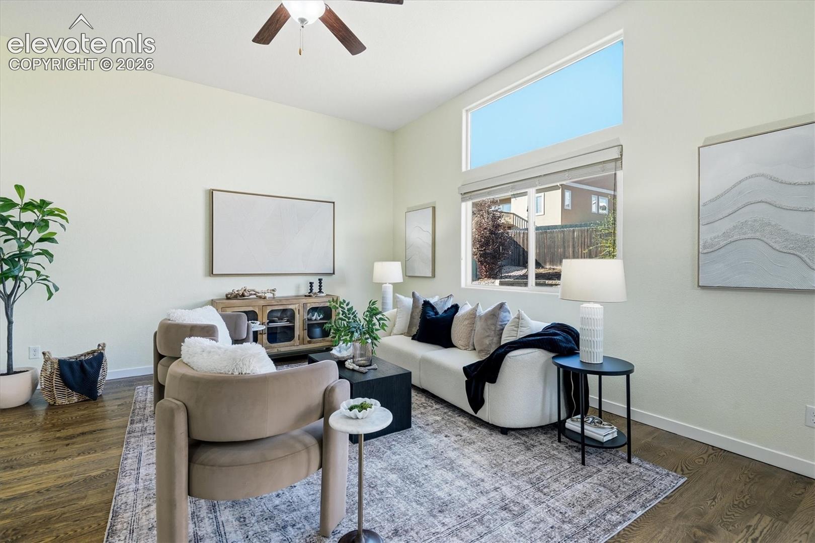 Vaulted ceiling with an attached ceiling fan, large windows with upper transom, wood-finish flooring, and light-toned walls