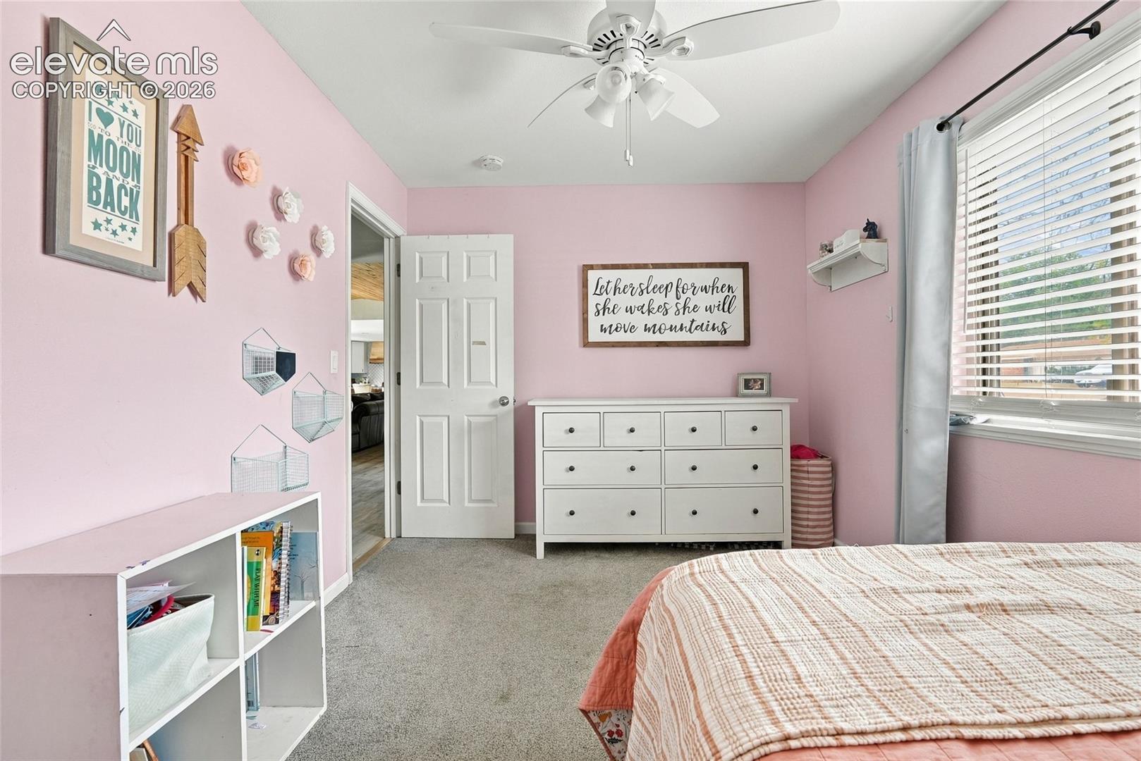 White five-panel interior door, ceiling fan with light fixture, window with horizontal blinds, built-in shelving unit, and carpeted flooring