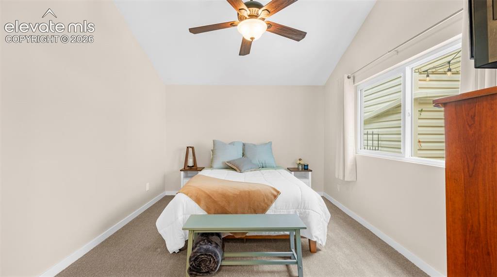 Bright room featuring a vaulted ceiling with a ceiling fan, carpeted flooring, and a large window providing natural light
