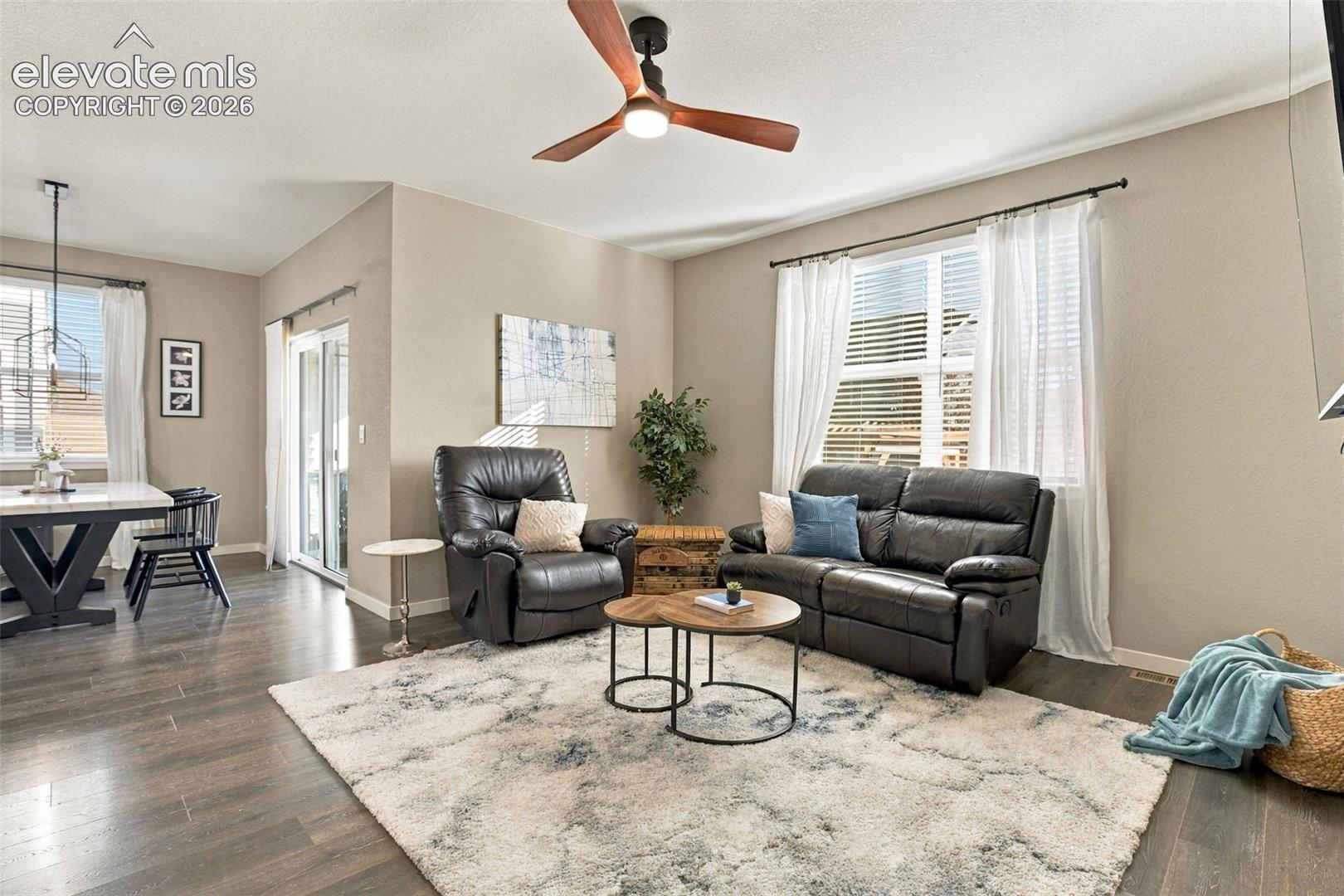 Living space featuring wood-finish flooring, a contemporary three-blade ceiling fan with integrated lighting, a sliding glass door, and large windows with horizontal blinds