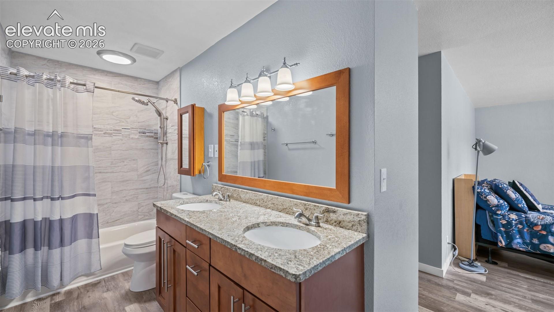 Bathroom featuring a double vanity with stone-finish countertop, wood-finish cabinetry, and contemporary light fixture
