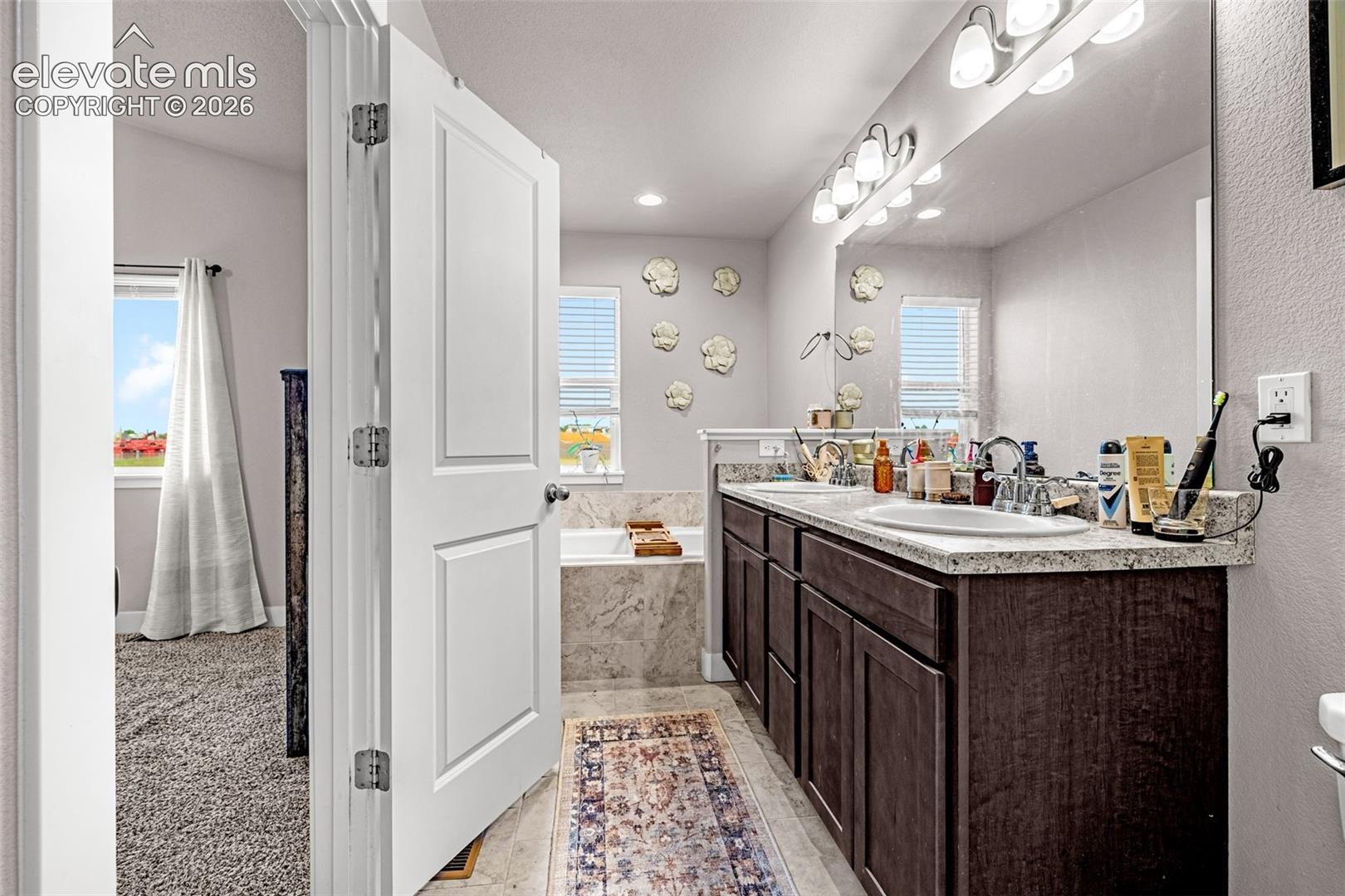 Spacious bathroom featuring a double vanity with ample counter space, dark wood cabinetry, and an integrated soaking tub
