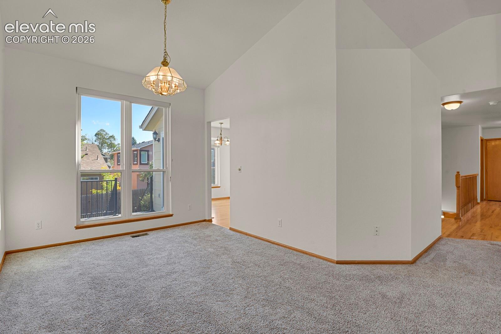 Vaulted ceiling, pendant light fixture, large window, carpeted flooring, wood trim