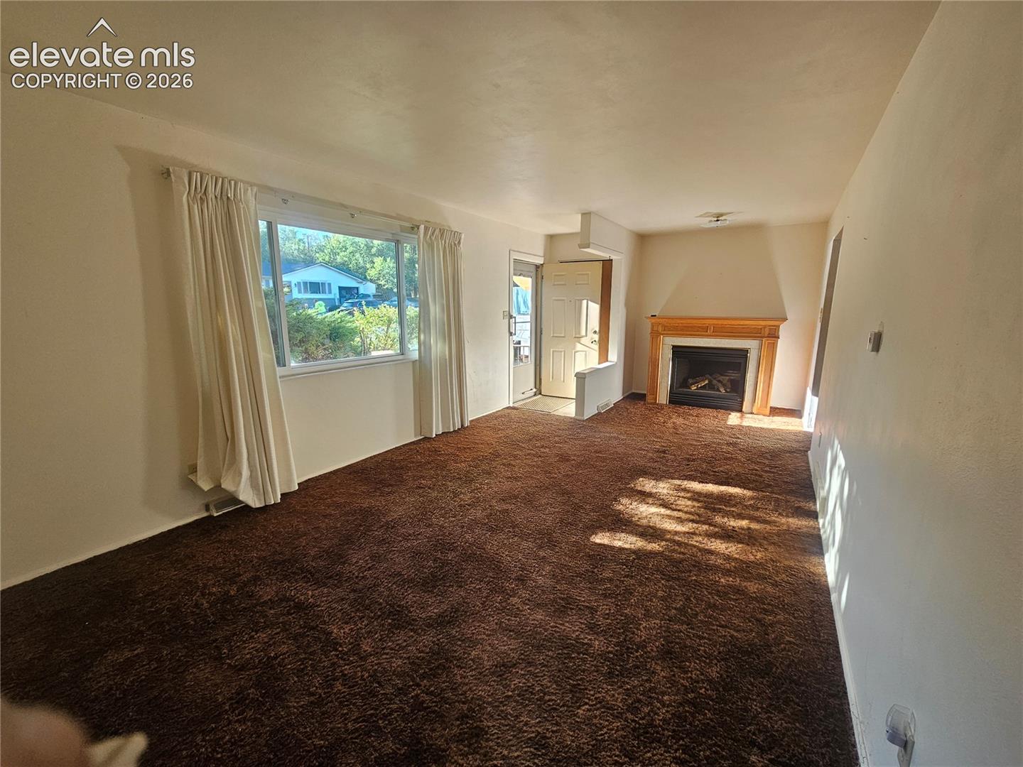Spacious room, large window, and a fireplace with a wood mantel