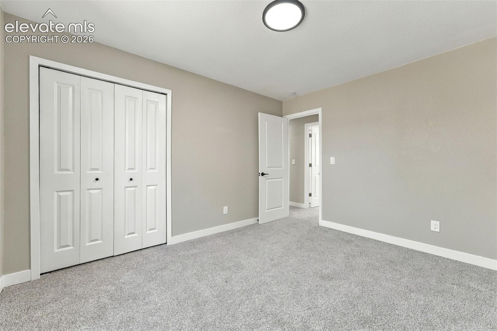 Neutral-toned interior featuring wall-to-wall carpeting, bi-fold closet doors, a multi-panel interior door, and a flush-mount circular ceiling light