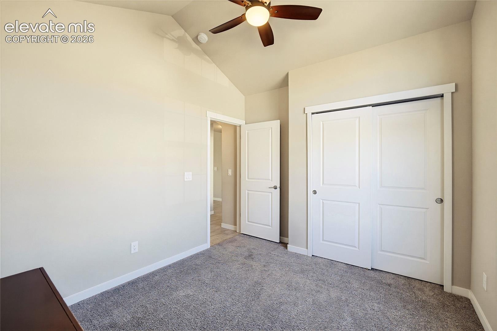 Vaulted ceiling featuring a central lighted ceiling fan, carpeted flooring, and a double-door closet with recessed paneling