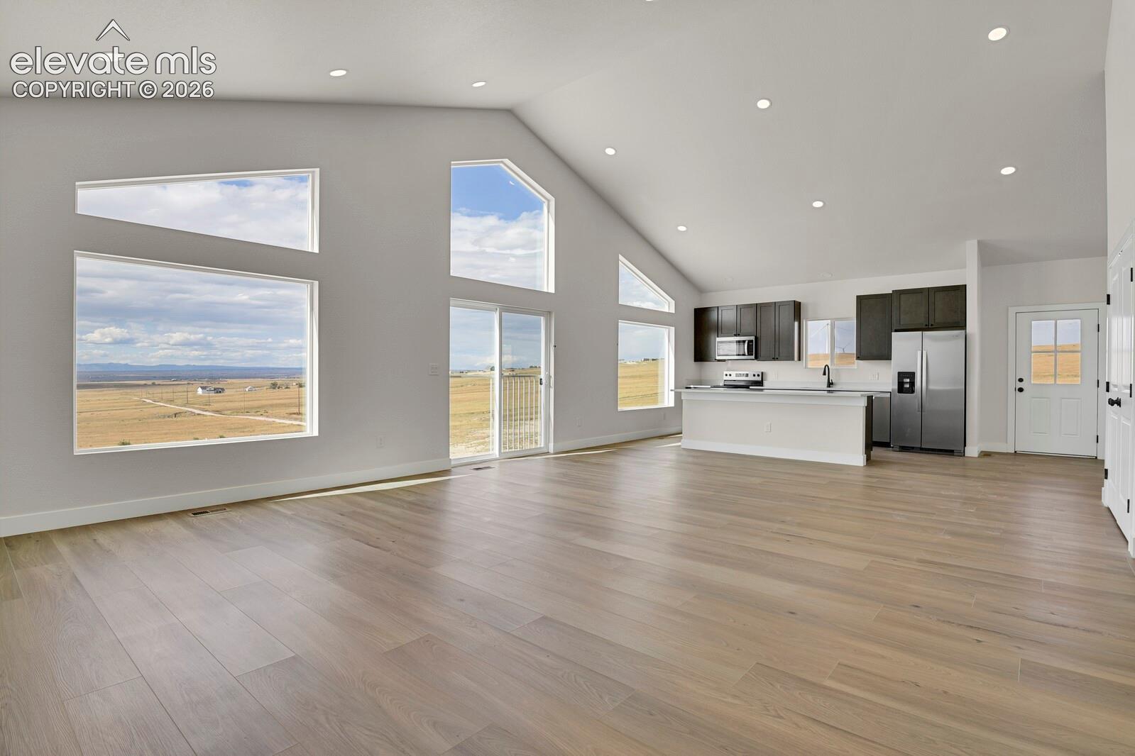 Open-concept floor plan featuring vaulted ceilings, wood-finish flooring, recessed lighting, and expansive floor-to-ceiling windows