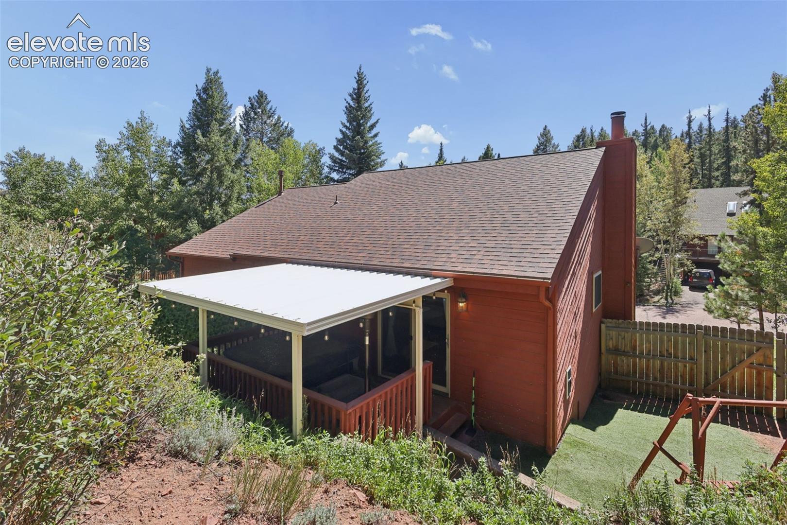 Red siding exterior, covered deck with railings, brown shingle roof, and a visible chimney