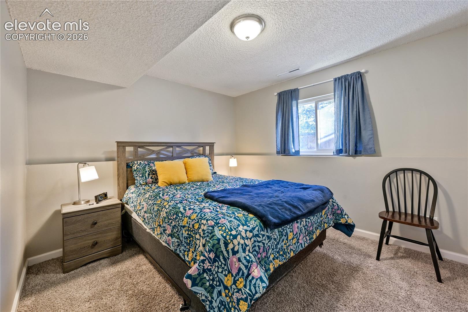 Neutral-toned room featuring textured ceiling, neutral wall paint, carpeting, and a single window with a curtain rod