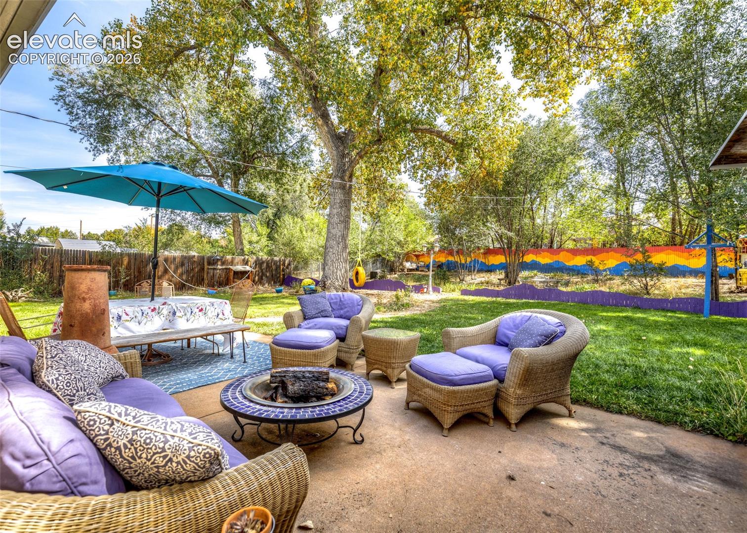 Expansive outdoor patio with concrete surfacing, a built-in fire pit, and mature shade trees