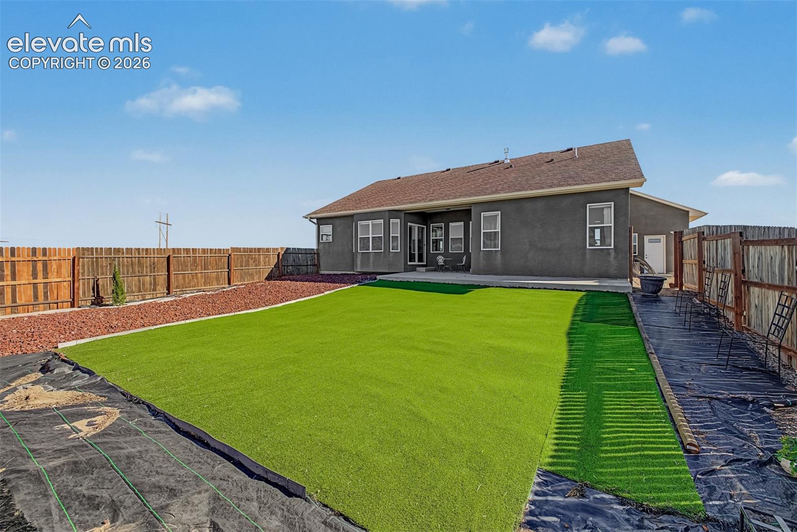 Rear exterior featuring a synthetic lawn, concrete patio and perimeter wood fencing.