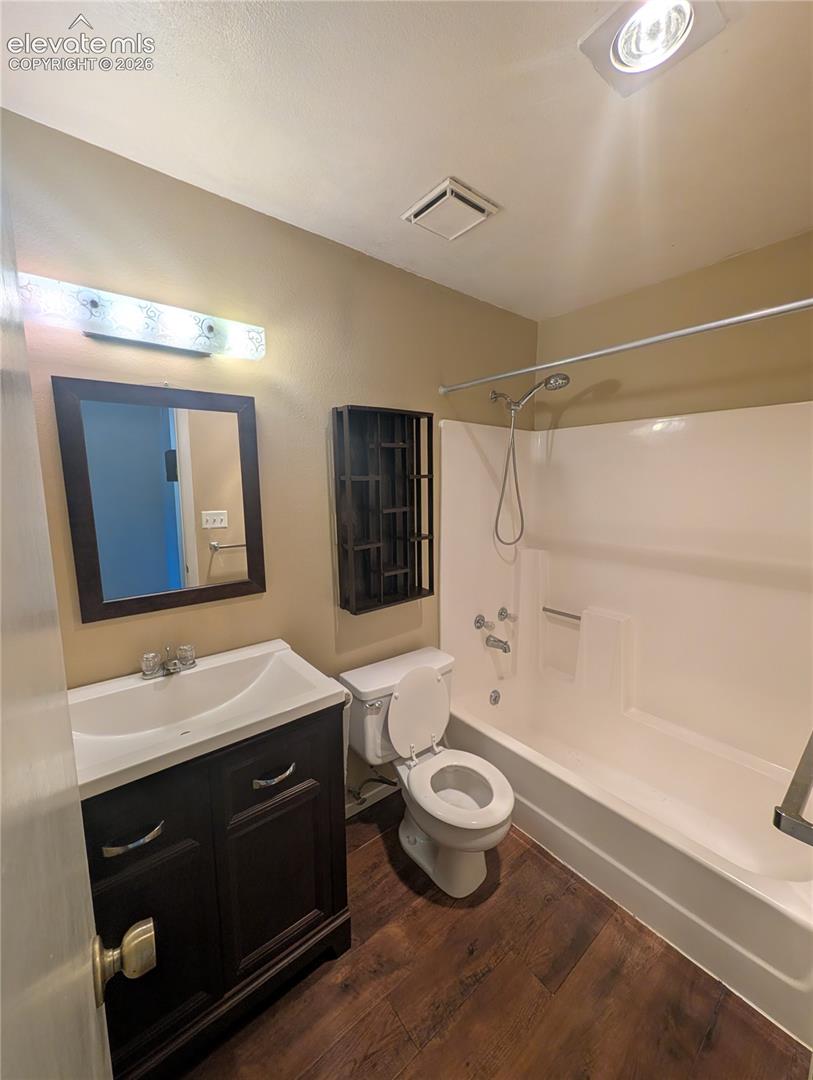 Wood-finish flooring, dark wood-finish vanity with an integrated sink, framed mirror, and a white bathtub with a shower head