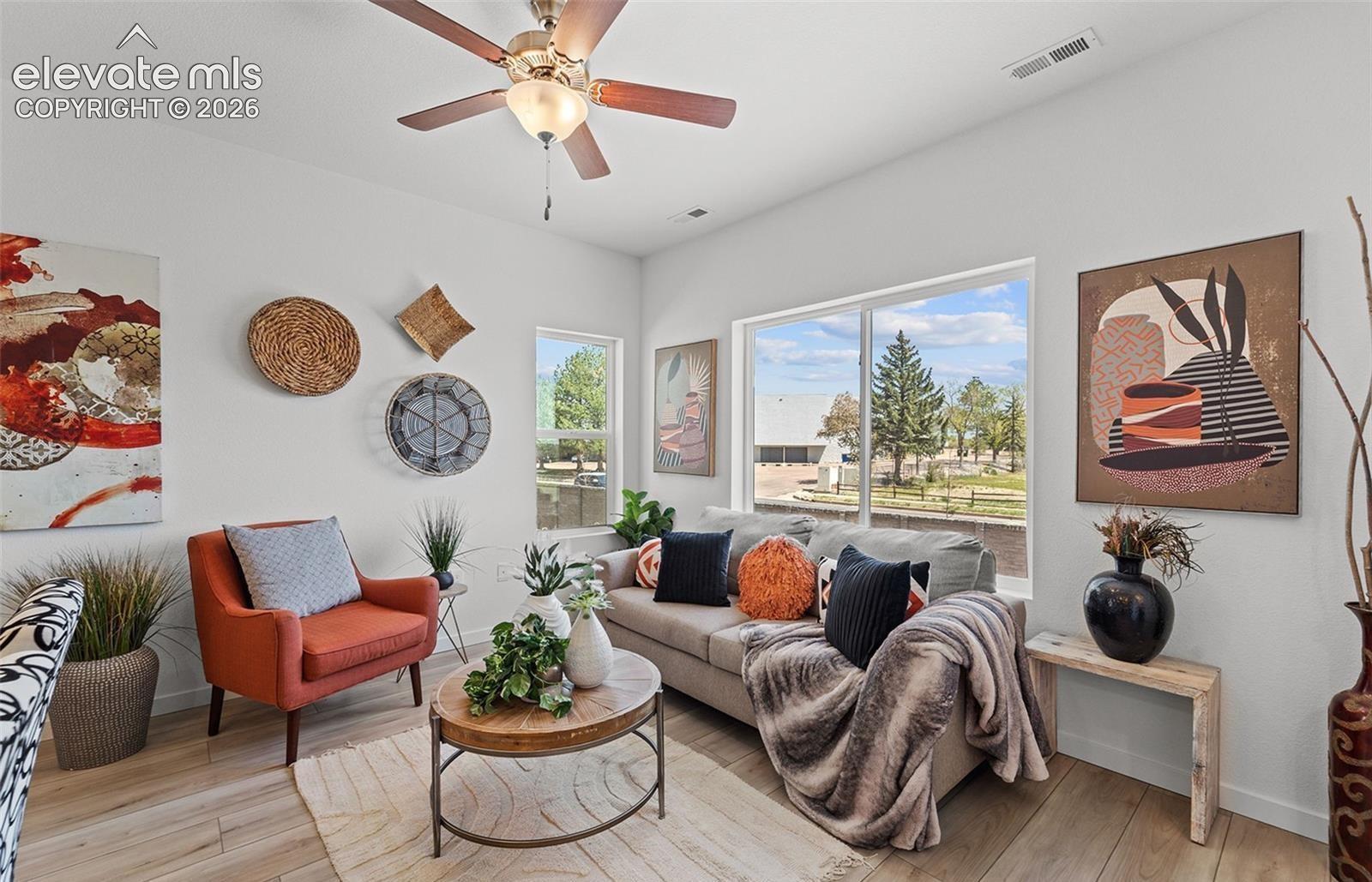 Living area featuring wood-finish flooring, high ceilings, a ceiling fan with integrated lighting, and large windows providing natural light