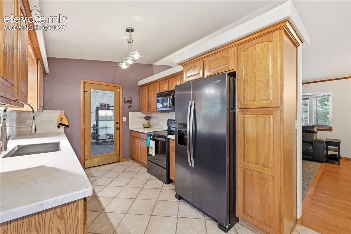 Kitchen featuring wood cabinetry, white countertops, stainless steel refrigerator, black range, and tile flooring