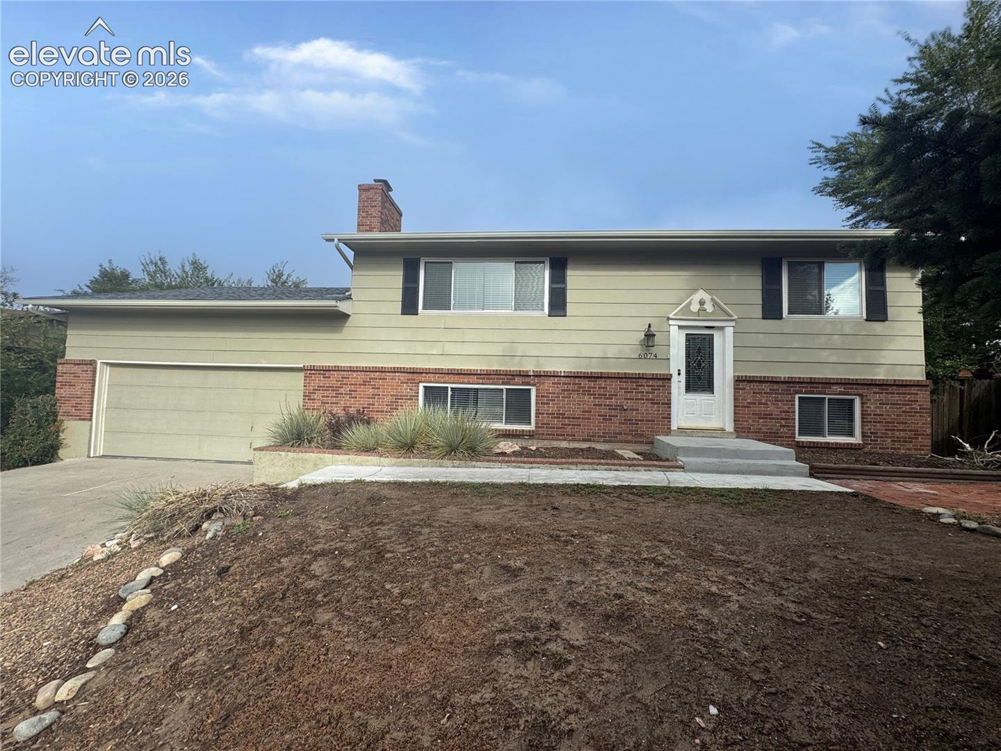 Split-level exterior featuring a combination of brick and horizontal siding, an attached two-car garage, a brick chimney, and a decorative front door surround