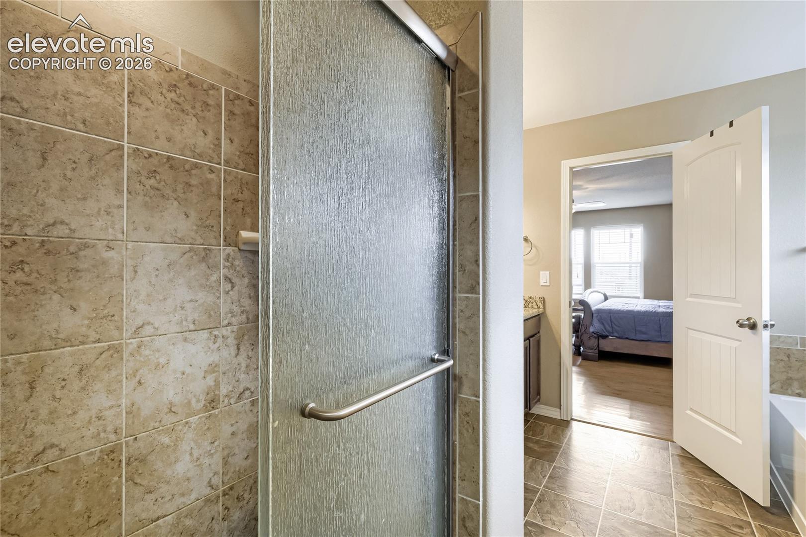 Walk-in shower featuring a textured glass door and large format tile surround