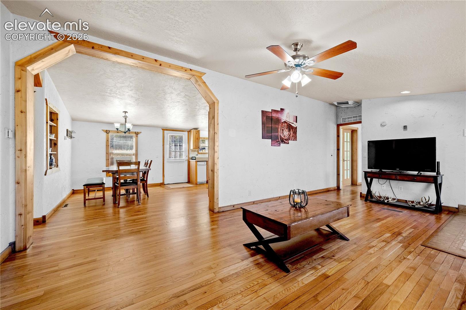 Living room featuring a textured ceiling, ceiling fan with notable chandelier, light wood-type flooring, and built in shelves