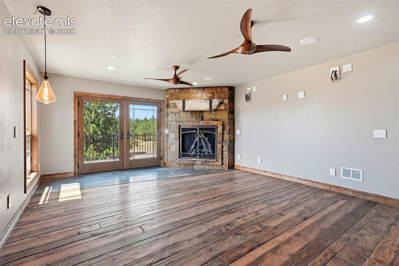 Spacious room featuring wood-finish flooring, a corner stone fireplace, and double French doors opening to a balcony