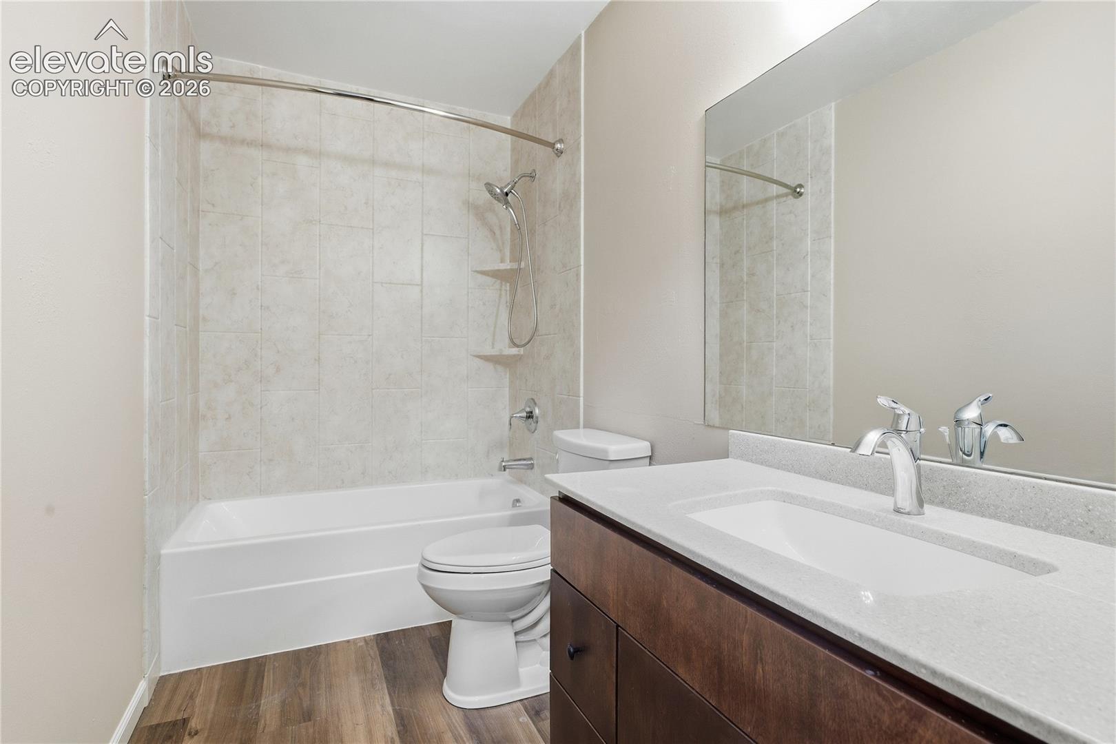 Full-size mirror, single vanity with integrated sink, chrome faucet, bathtub with shower, and wood-finish flooring