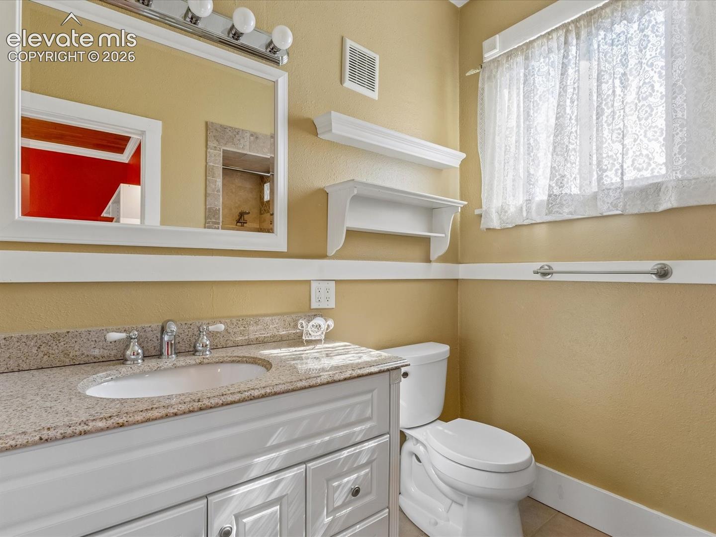 Bathroom vanity featuring a light-colored stone-finish countertop with an undermount sink and chrome faucet