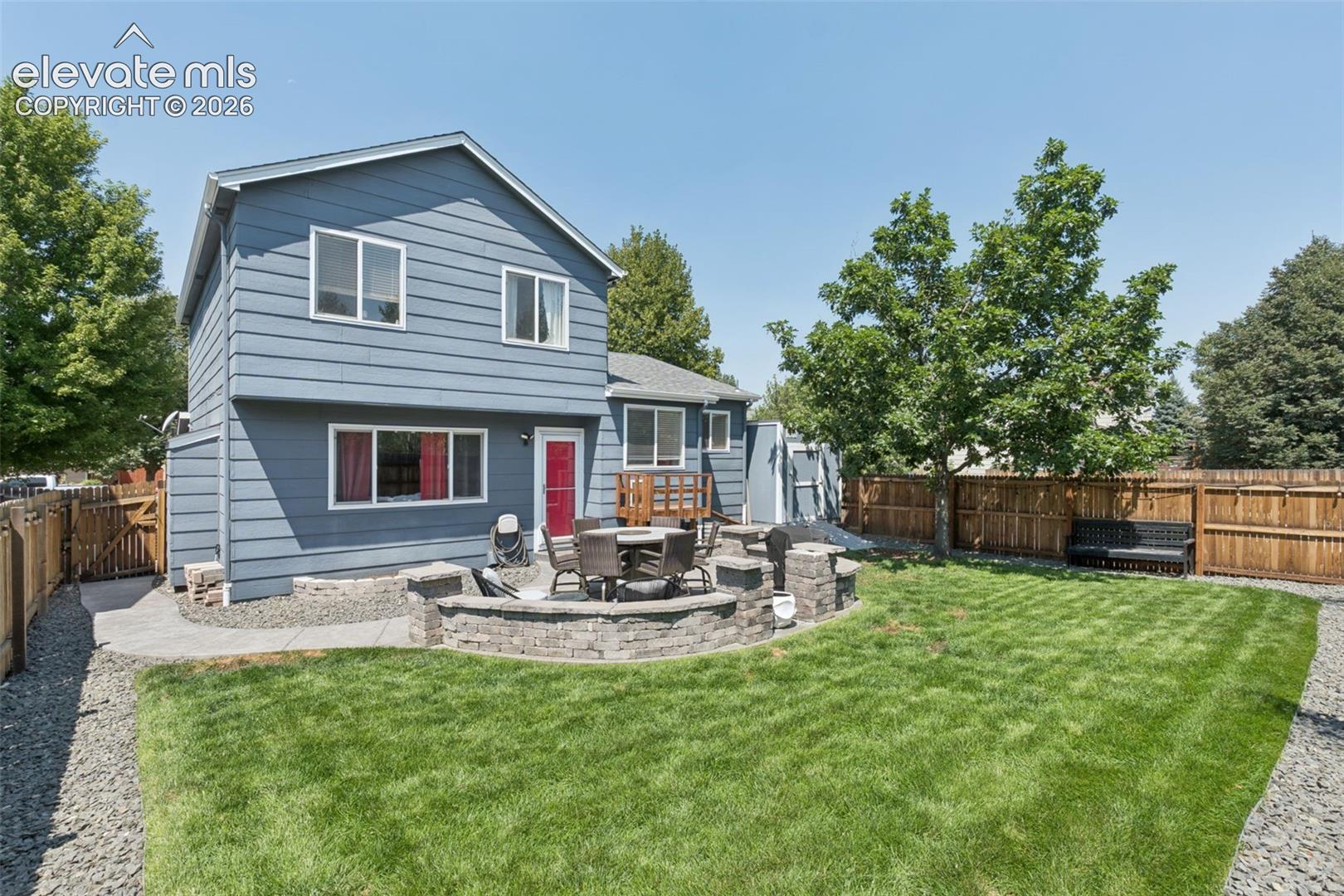 Expansive backyard featuring a manicured lawn, established perimeter fencing, and a paver patio with a stone-finish retaining wall