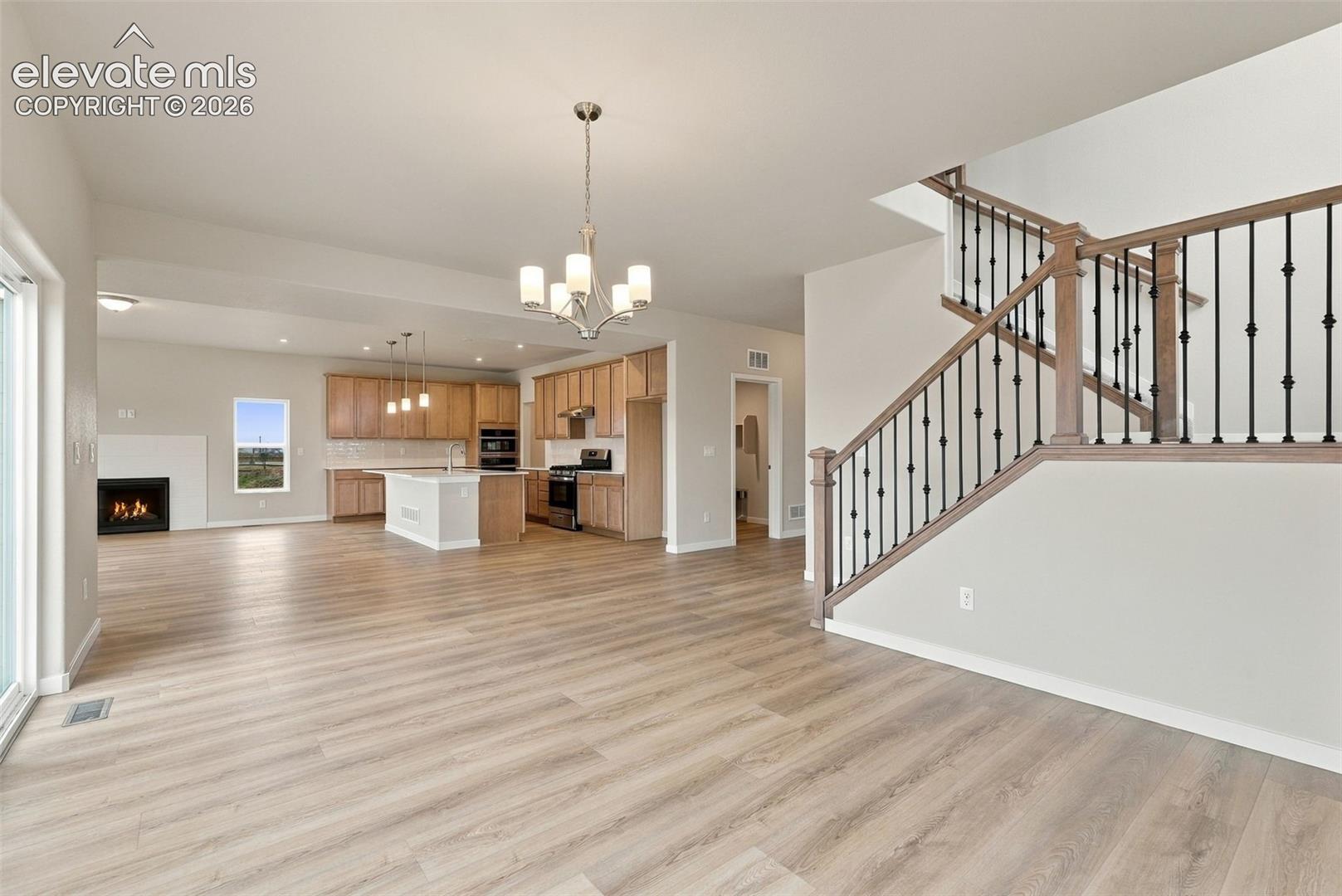 Open-concept interior featuring wood-finish flooring, a central kitchen island with cabinetry, a built-in fireplace, and a staircase with metal balusters and wood handrails