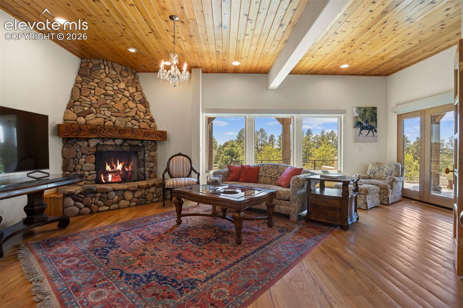 The den features a Dramatic floor-to-ceiling stacked river stone wood-burning fireplace with artisan hand-carved wood mantle.