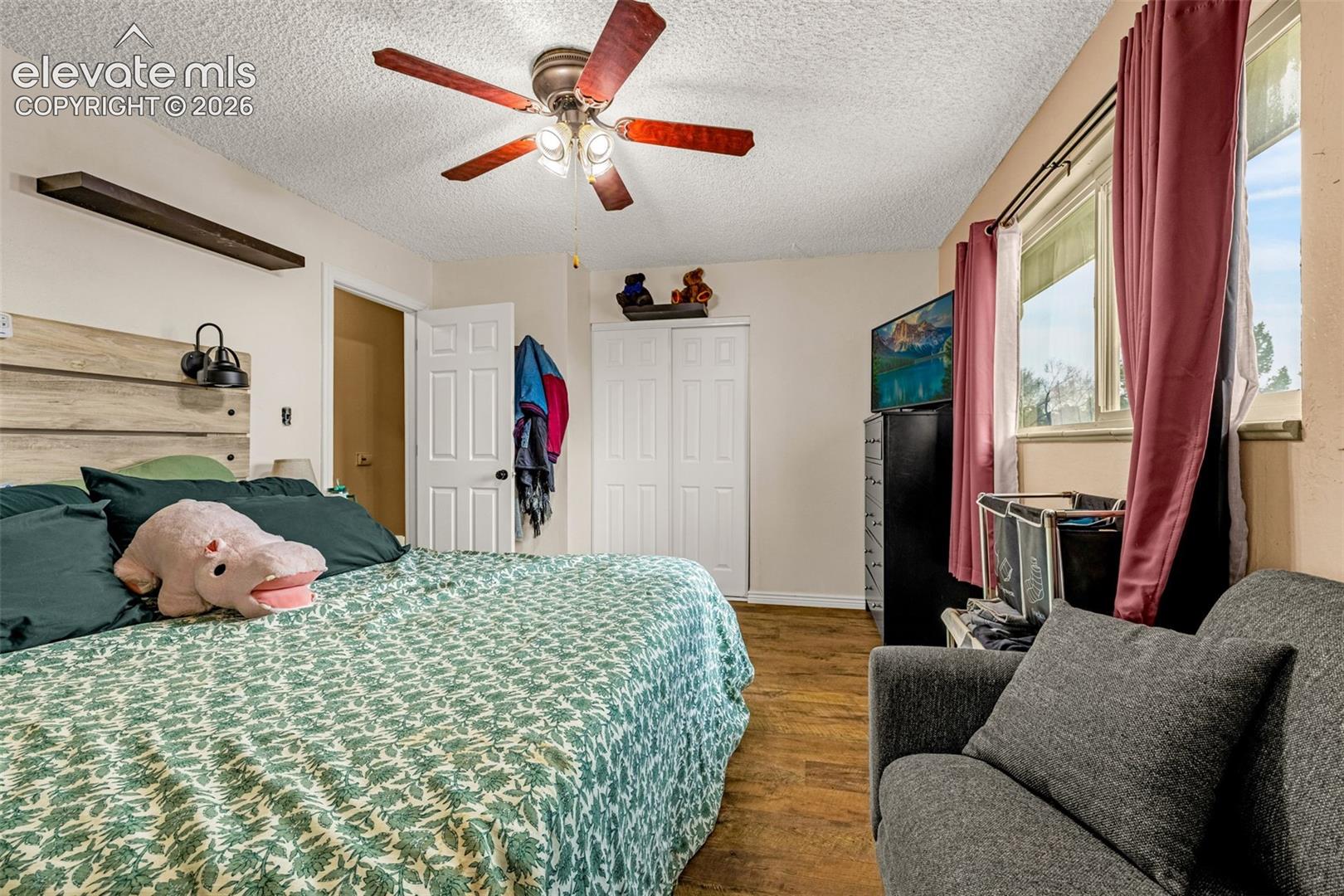 Room featuring wood-finish flooring, a ceiling fan with integrated lighting, a built-in horizontal wall shelf, and a dual-panel closet