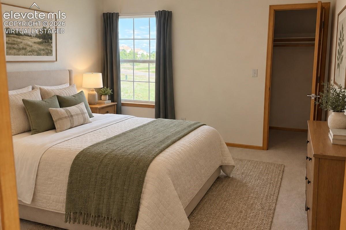Upstairs Bedroom 2/3 with walk-in closet, featuring a large window with grid panes, neutral carpeting, and a wood-finish doorway. Virtually staged.