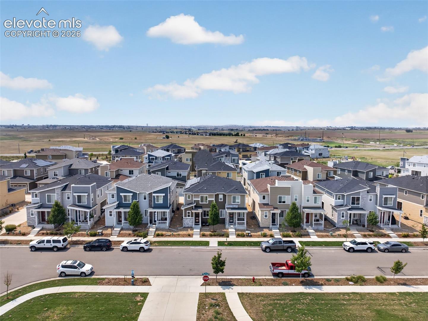 Aerial perspective of a planned community featuring multi-level residential properties, paved streets, concrete sidewalks, and landscaped front yards