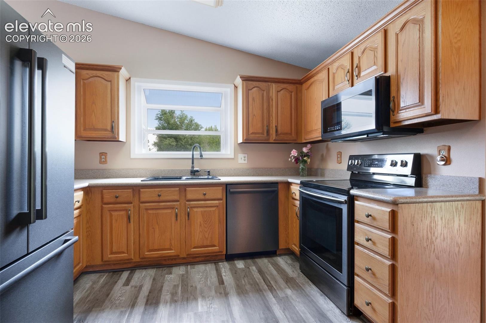 Kitchen with stainless steel appliances, lofted ceiling, a sink, light countertops, and light wood-style floors