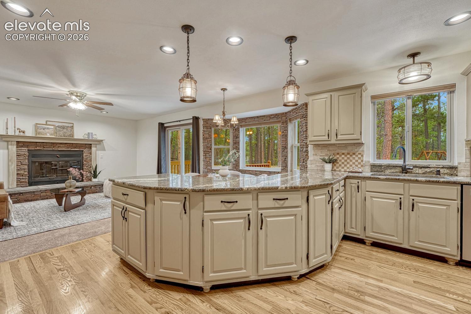 Kitchen featuring a large curved island, stone-accented hearth, wood-finish flooring, pendant lighting, and recessed ceiling lights