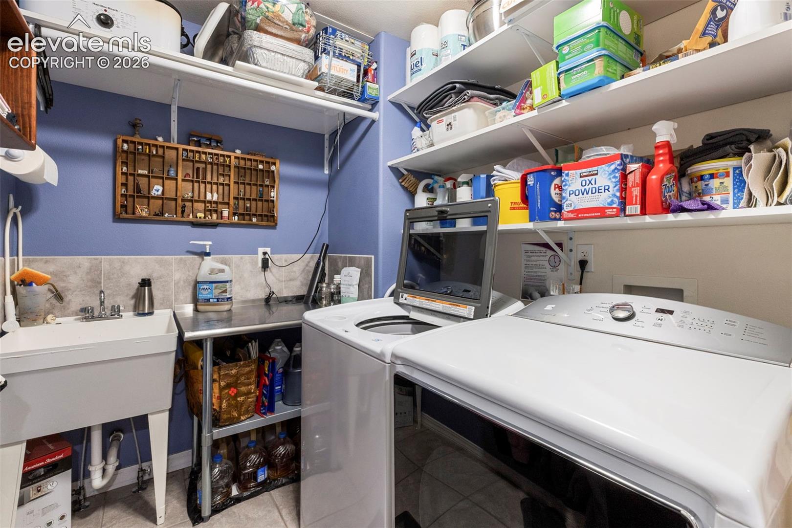 Utility room featuring a built-in sink, tiled backsplash, wall-mounted shelving, and a stainless steel utility table