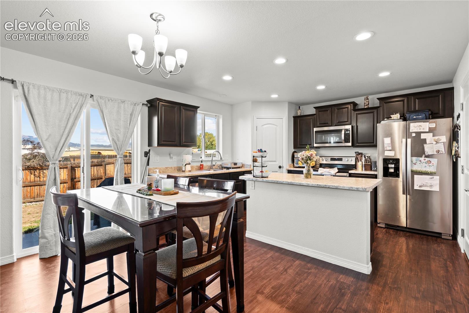 Kitchen featuring dark-finish cabinetry, stone-style countertops, wood-finish flooring, recessed lighting, and a breakfast bar