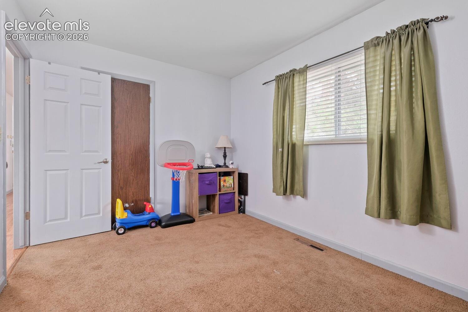 Carpeted room featuring a white paneled door, a dark wood-finish door, and a window with blinds