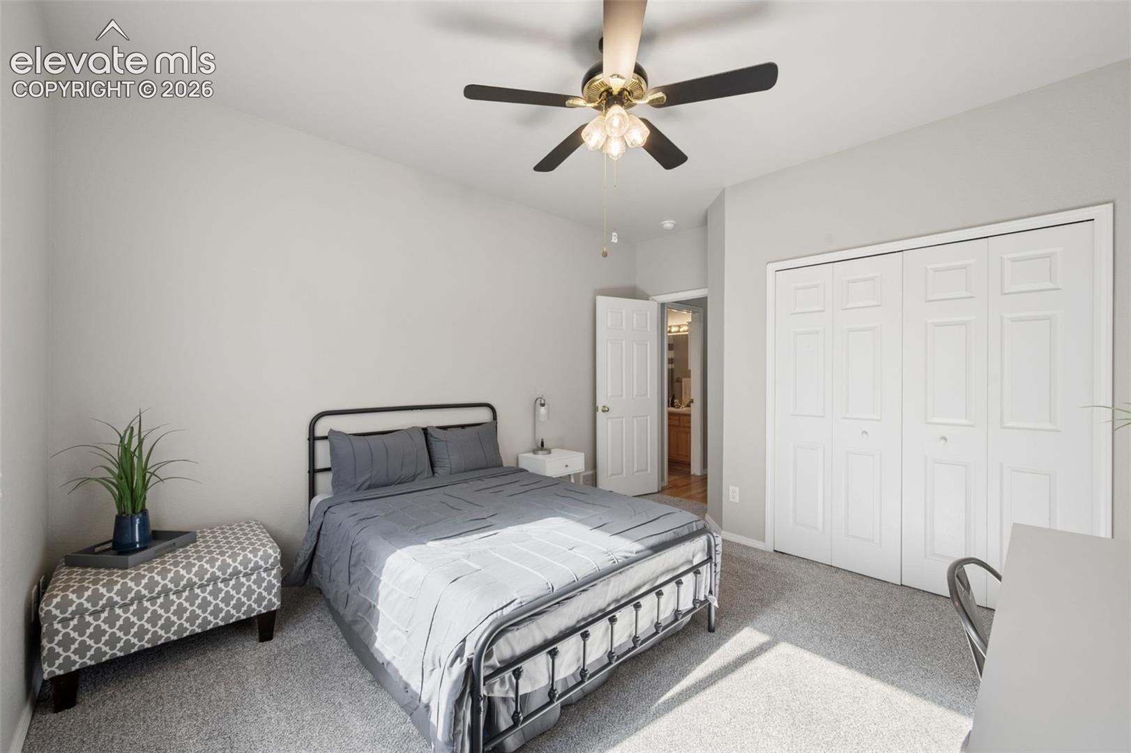 Neutral wall tones, carpeting, a ceiling-mounted light fixture with a fan, and a double-door reach-in closet