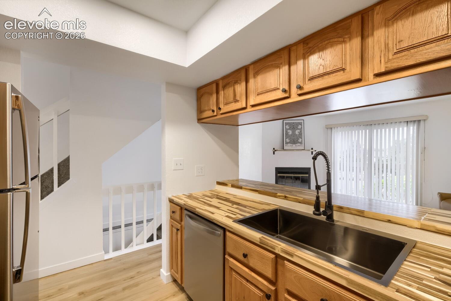 Kitchen featuring butcher block countertops, undermount rectangular sink with a pull-down faucet, stainless steel refrigerator, and wood cabinetry
