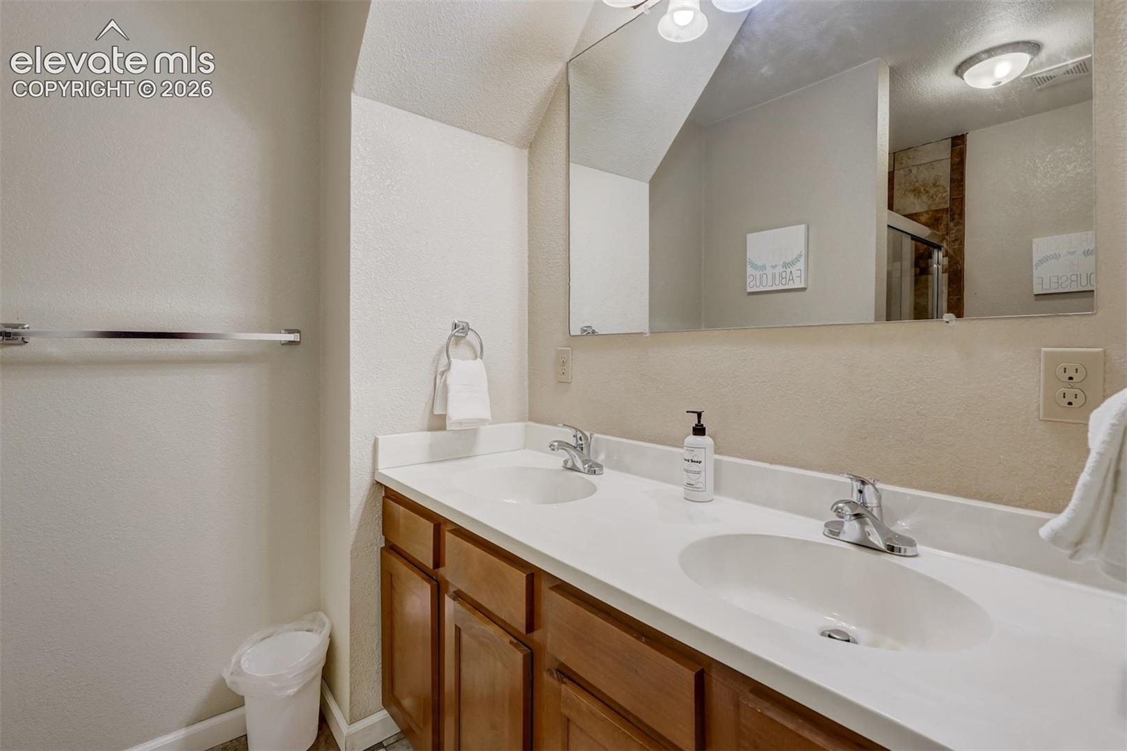 Dual vanity with integrated sinks and chrome fixtures, wood-finish cabinetry, and a large wall-mounted mirror