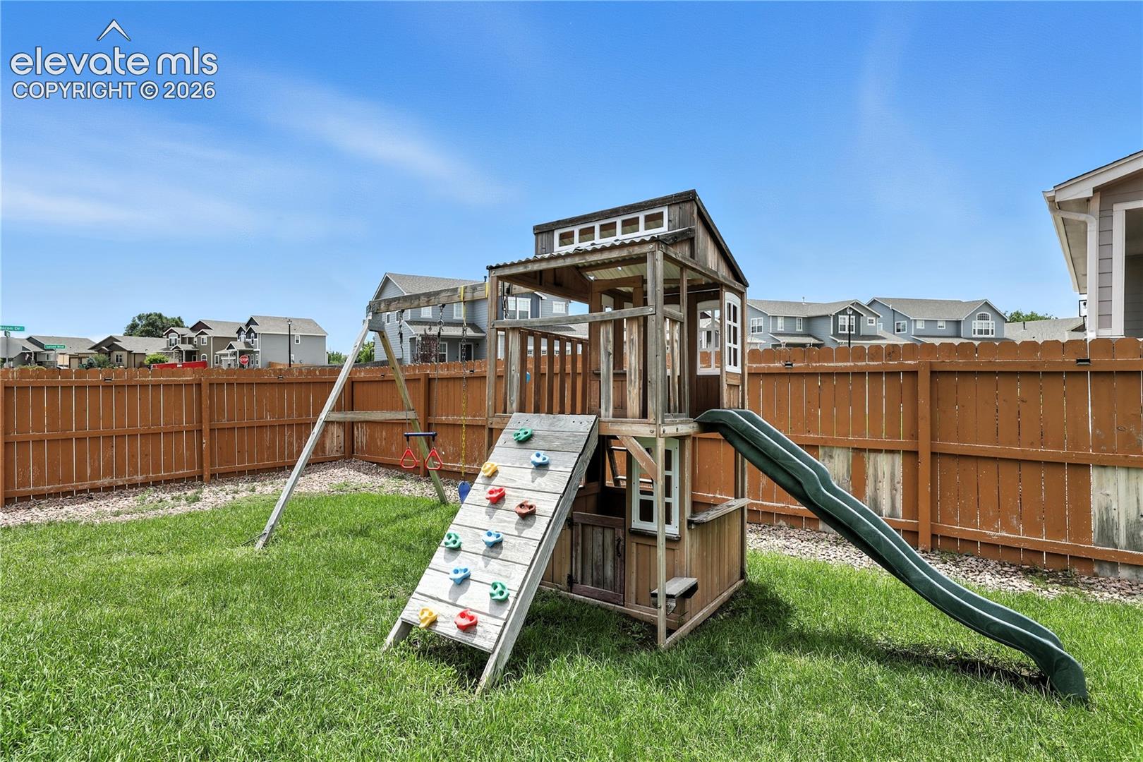 Fenced backyard featuring a manicured lawn, a wooden play structure, and a green slide