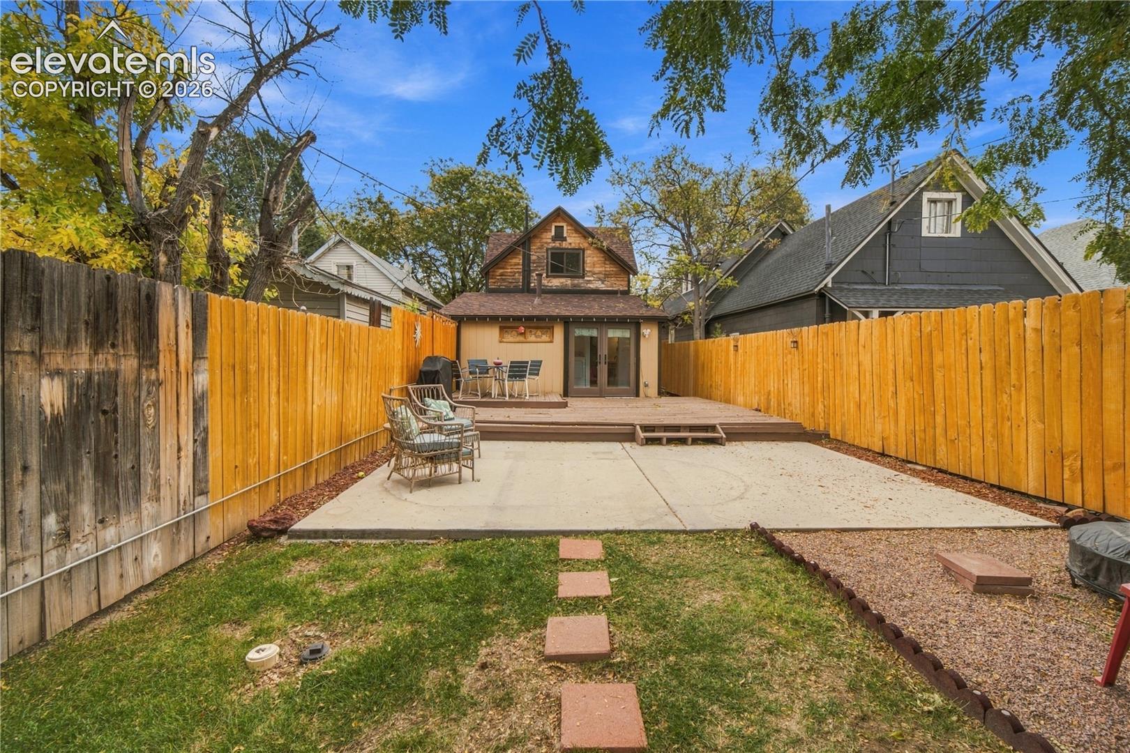 Fenced-in backyard featuring a concrete patio, wood deck, and stone paver walkway