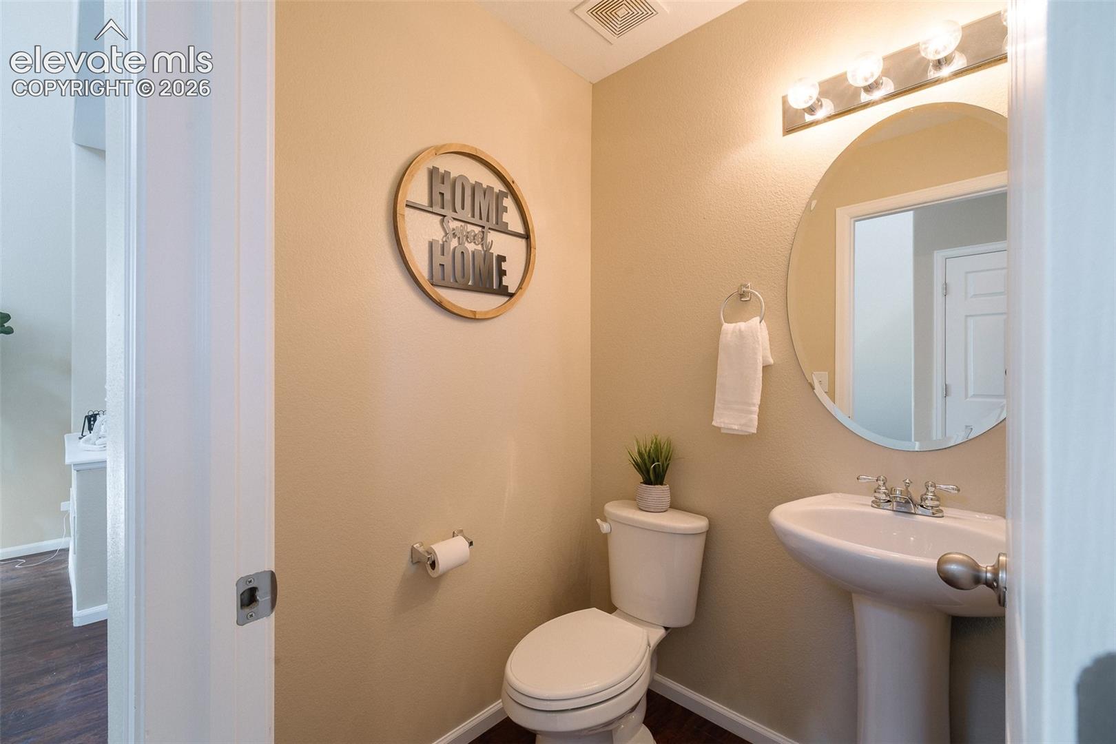 Pedestal sink with polished chrome dual-handle faucet, large circular frameless mirror, and multi-bulb integrated vanity lighting