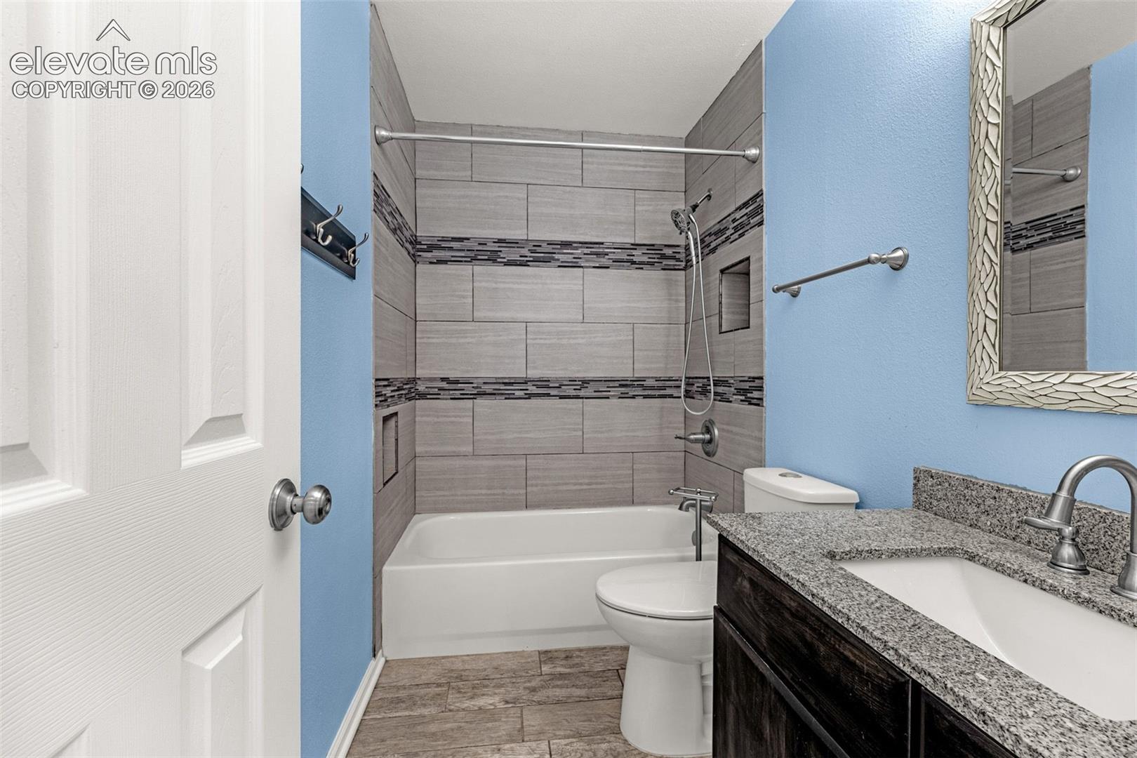 Bathroom featuring a stone-finish countertop with an integrated basin, dark wood-finish cabinetry, a built-in recessed shower niche, and horizontal tile wall surrounds with a decorative mosaic accent band