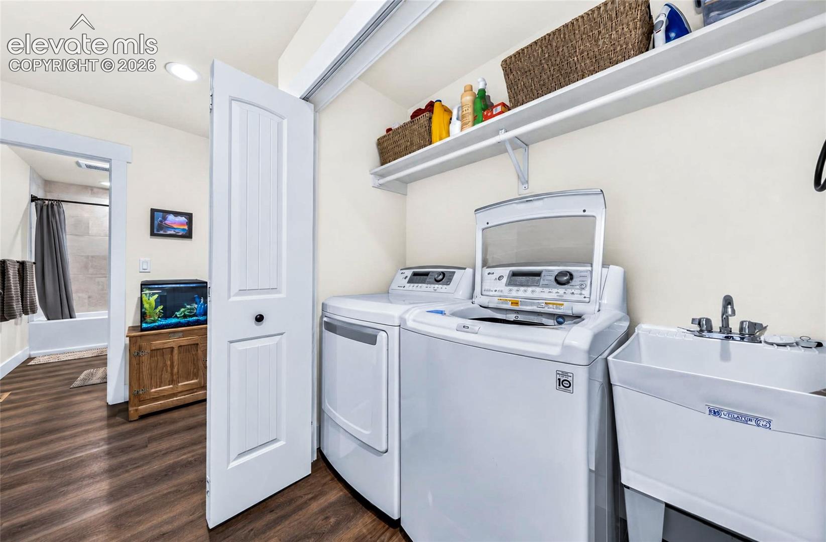 Laundry room featuring wood-finish flooring, a utility sink with dual-handle faucet, and built-in upper shelving